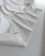 Camicia bianca elegante in cotone, piegata con attenzione ai dettagli e stile minimalista.