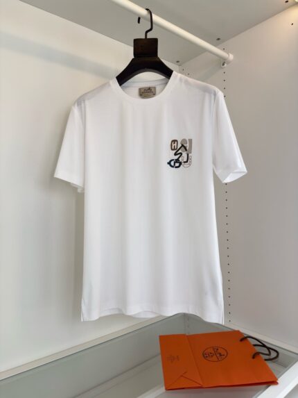 T-shirt bianca minimalista con ricamo moderno, accompagnata da borsa arancione branding.