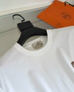 T-shirt bianca elegante con dettaglio grafico e accessorio di lusso in ambiente raffinato.