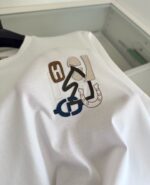 Maglietta bianca con ricami artistici, simboli moderni e dettagli colorati, stile casual elegante.