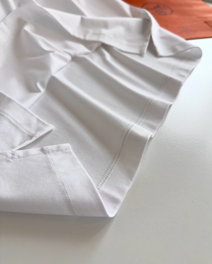 Camicia bianca elegante con colletto rifinito e dettaglio di tessuto arancione vibrante.