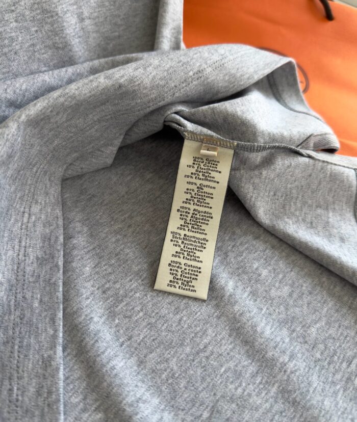 Maglietta grigia con etichetta su sfondo arancione, stile casual e moderno.