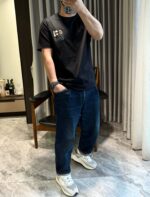 Persona rilassata con t-shirt nera, jeans e sneakers bianchi in ambiente domestico.
