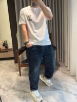 Stile casual con jeans, t-shirt grafico e sneakers bianche in ambiente domestico.