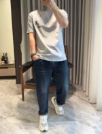 Persona in abbigliamento casual con jeans distressed e sneakers bianche in ambiente rilassato.