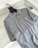 Maglietta polo grigia con logo, collo con bordino bianco e design minimalista elegante.