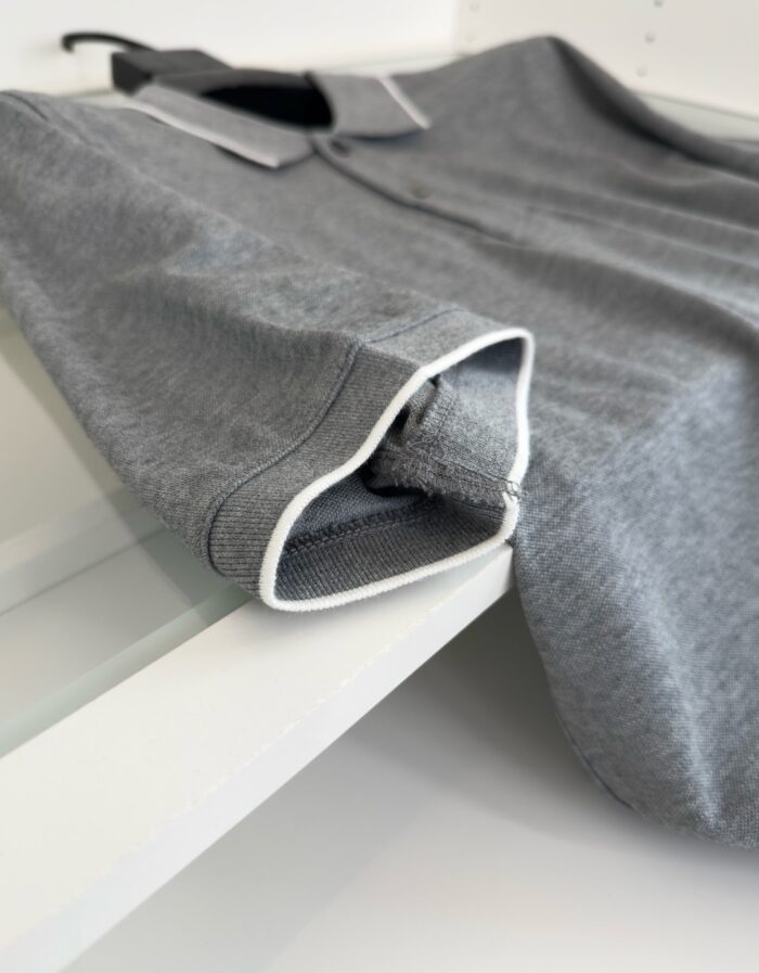 Maglietta polo grigia con piping bianco, elegante e versatile, perfetta per look casual e semi-formali.