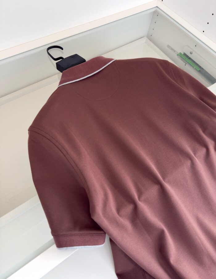 Maglietta polo bordeaux eleganti su appendiabiti, stile casual e raffinato in ambiente ordinato.