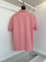 Maglietta polo rosa chiaro su gruccia in ambiente minimalista e luminoso.