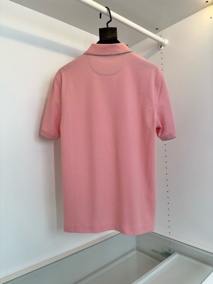 Maglietta polo rosa chiaro su gruccia in ambiente minimalista e luminoso.