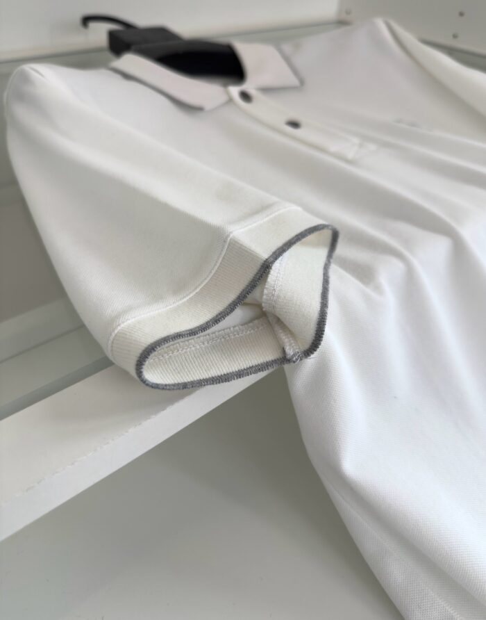 Maglietta polo bianca con colletto e righe a contrasto, stile casual ed elegante.