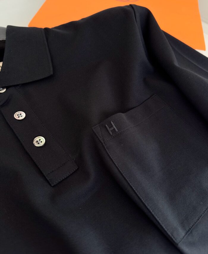 Maglietta polo nera elegante con taschino, sfondo arancione vibrante, stile casual e sofisticato.