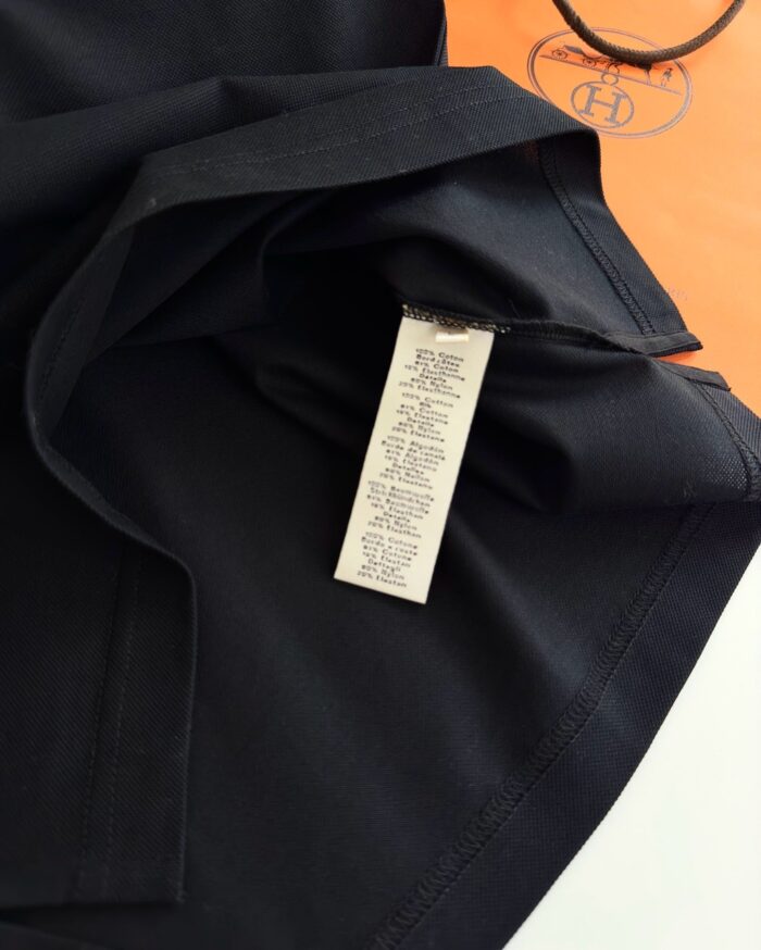 Dettaglio di vestito nero con etichetta elegante su sfondo arancione vibrante.