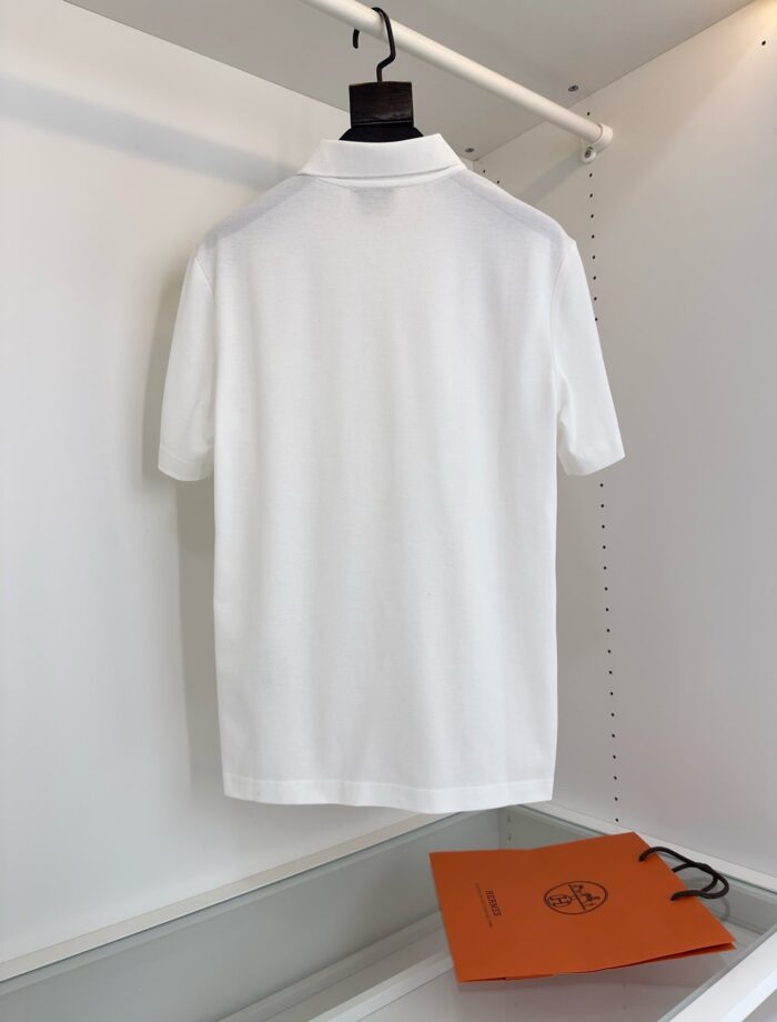 Poloshirt bianco di alta qualità con logo, elegante e minimalista, accompagnato da shopping bag arancione.