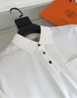 Camicia polo bianca elegante con dettagli raffinati, accompagnata da shopping bag arancione di lusso