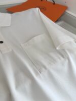 Maglietta polo bianca con taschino, sfondo con borsa arancione, stile casual elegante.
