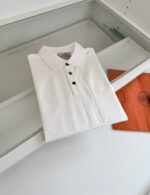 Maglietta polo bianca con dettagli arancioni, presentata in modo elegante e moderno.