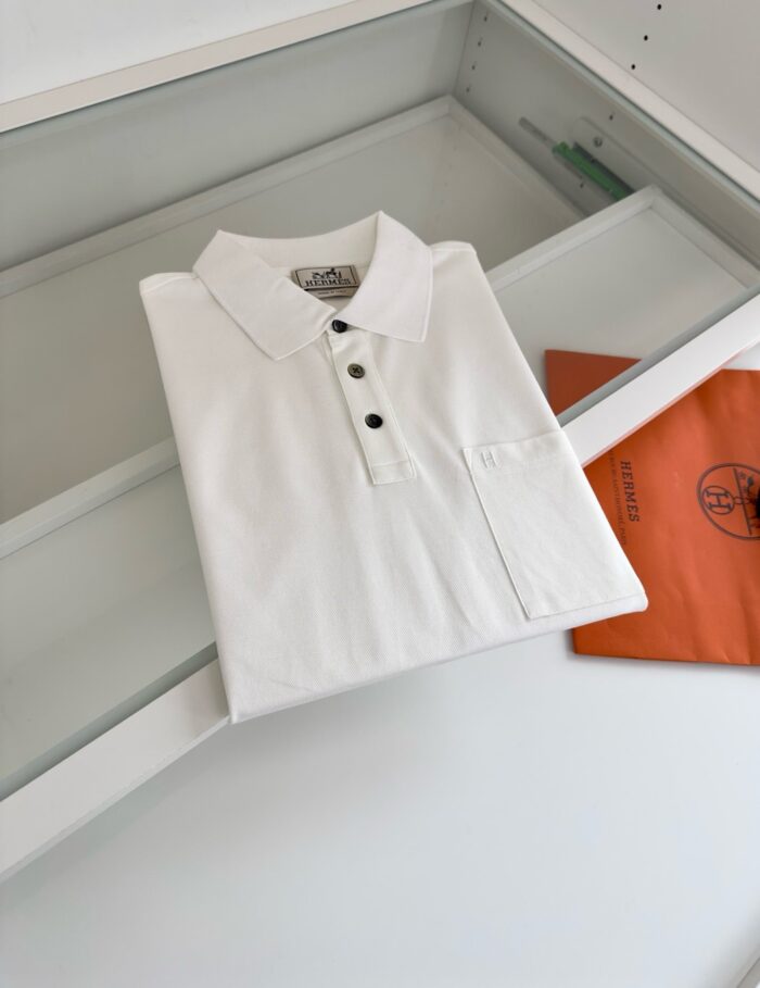 Maglietta polo bianca con dettagli arancioni, presentata in modo elegante e moderno.