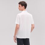Uomo con polo bianca elegante, stile casual e moderno, sfondo grigio neutro.