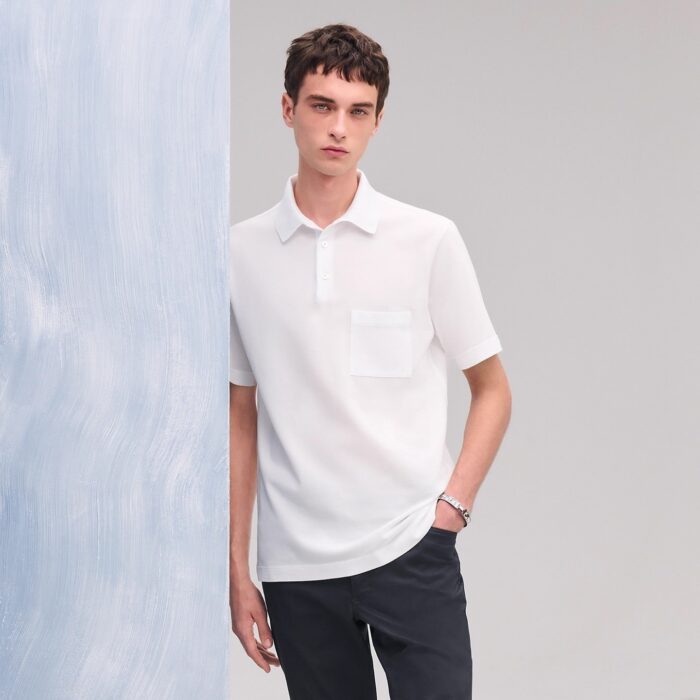 Ragazzo moderno in polo bianca e pantaloni scuri su sfondo blu tenue.