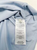 Camicia azzurra in cotone con etichetta di cura e dettagli di colore e qualità.