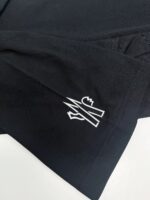 Maglietta nera con logo geometrico bianco sul polsino, stile moderno e minimalista.