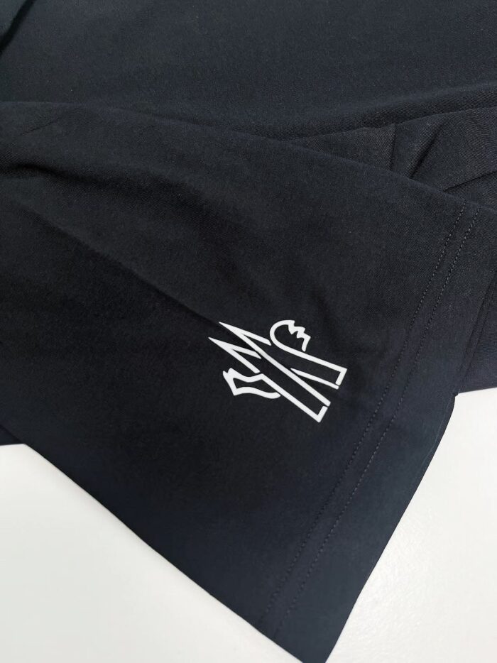 Maglietta nera con logo geometrico bianco sul polsino, stile moderno e minimalista.