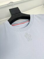 Maglietta blu chiara, logo minimale, dettaglio interno a strisce rosso, bianco e blu.