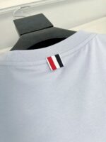 Maglietta celeste con dettaglio logo sottocollare in stile preppy e hanger in legno nero.