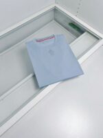 Maglietta azzurra minimalista con dettaglio a strisce rosso, bianco e blu, in esposizione elegante.