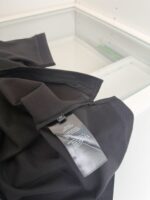 T-shirt nera con etichetta, pieghe e cura in ambiente minimalista.