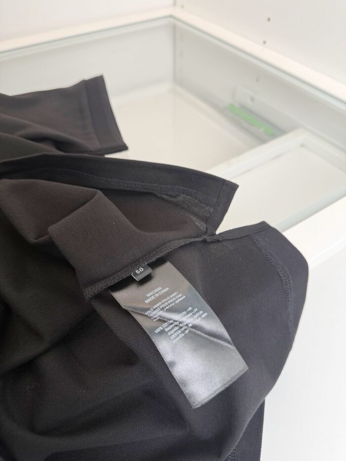 T-shirt nera con etichetta, pieghe e cura in ambiente minimalista.