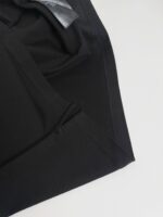 Dettaglio di tessuto nero elasticizzato con cuciture precise e etichetta discreta, elegante e versatile.