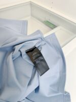 Vestito in cotone blu con etichetta di cura su sfondo minimalista e naturale.