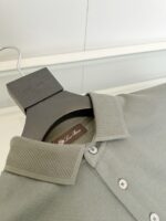 Maglietta polo grigia elegante in cotone su appendiabiti nero, stile minimalista e raffinato.