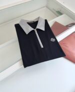 Maglietta polo nera con colletto grigio, zip frontale e logo ricamato, stile moderno ed elegante.
