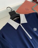 Maglietta polo navy con colletto grigio, zip frontale e logo sottile, stile elegante e casual.