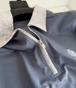 Maglietta polo moderna con colletto grigio, zip e logo ricamato, perfetta per sport e casual.