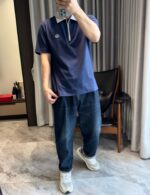 Persona in abbigliamento casual con jeans, polo navy e sneakers in ambiente moderno e minimalista.
