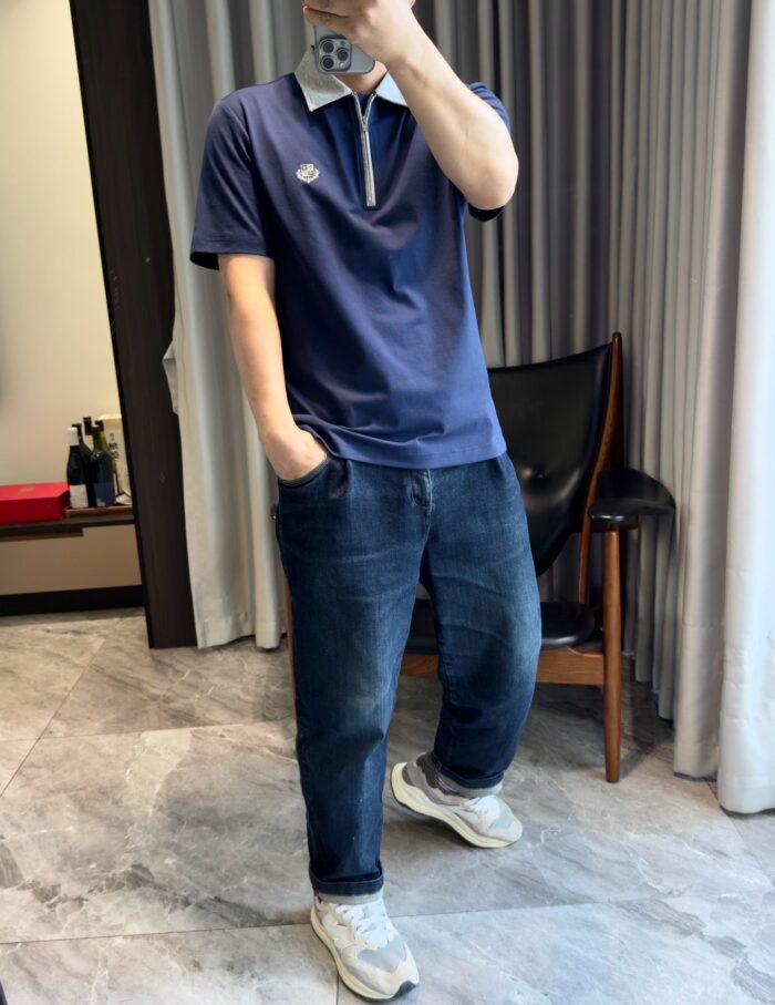 Uomo in stile casual con polo blu, jeans e sneakers bianche in interno moderno e luminoso.