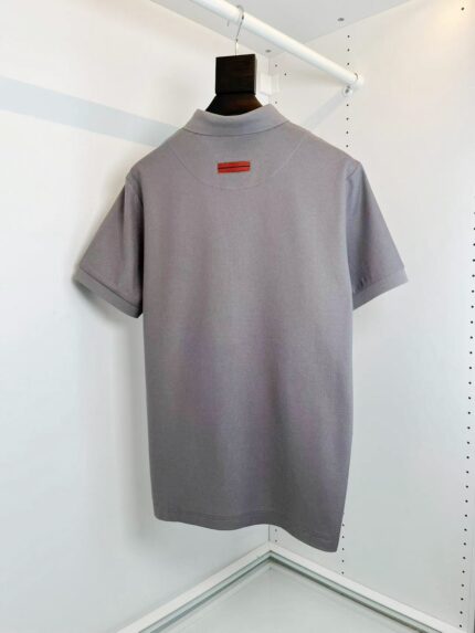 Polo grigia minimalista con dettaglio rosso sul tag, stile elegante e versatile per ogni look.