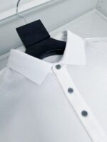Camicia bianca elegante con colletto classico, bottoni neri e design minimalista su appendiabiti nero.