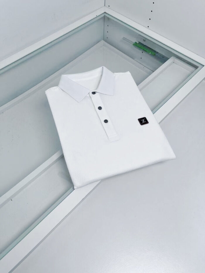 Maglietta polo bianca elegante con colletto a contrasto, esposta su display trasparente moderna.