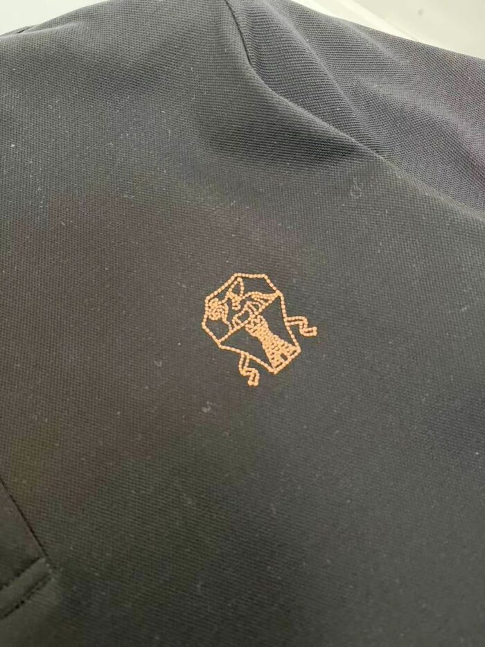 Giacca sportiva con logo stilizzato arancione e dettagli eleganti su tessuto scuro.