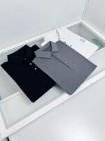 Magliette polo classiche nere, grigie e bianche su tavolo minimalista, stile casual e sofisticato.