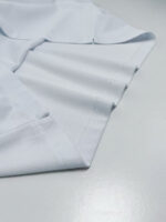 Camicia bianca piegata, cotone di alta qualità, dettagli curati, sfondo grigio elegante.