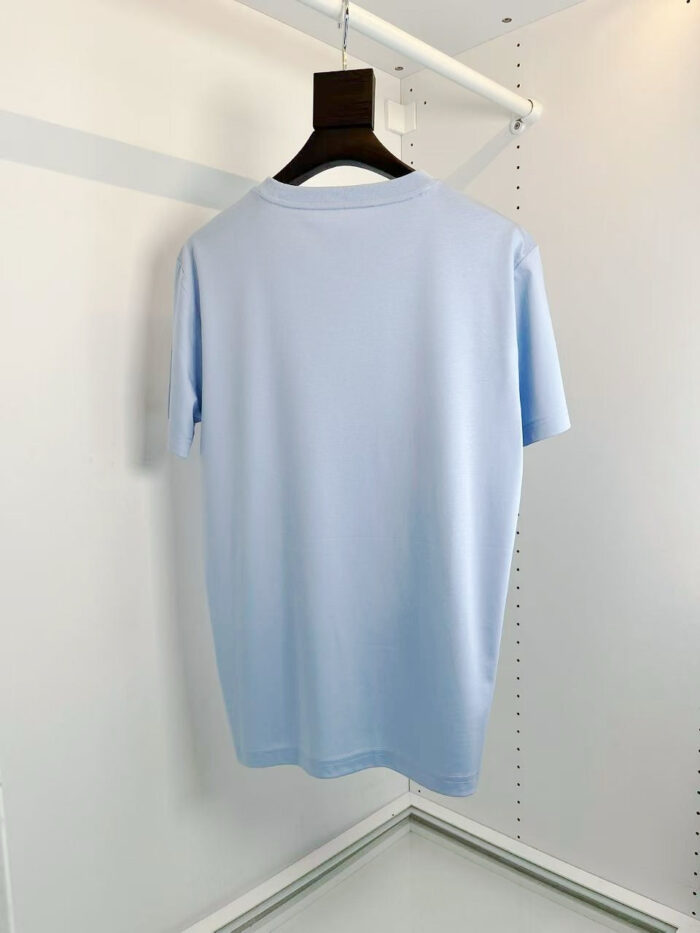 Maglietta blu pastello semplice su appendino in ambiente minimalista e luminoso.