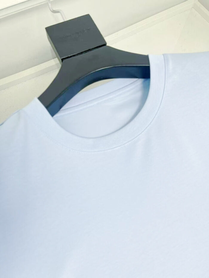 Maglietta casual blu chiaro su appendiabiti nero, tessuto morbido e leggero, stile semplice e moderno.