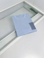 Maglietta celeste con taschino a motivo geometrico, stile casual e moderno.