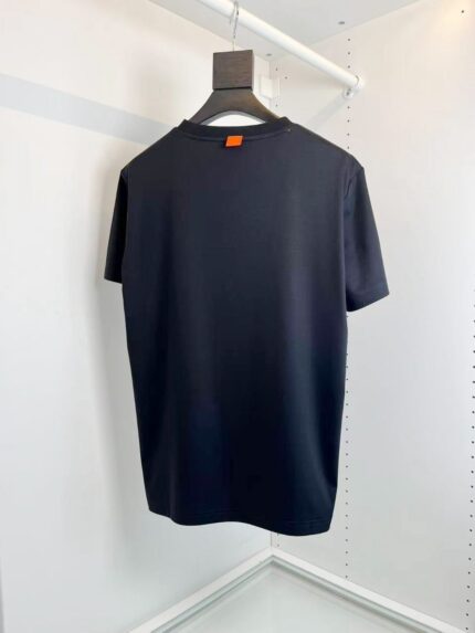 Maglietta nera minimalista con dettaglio arancione su appendiabiti di legno, elegante e versatile.